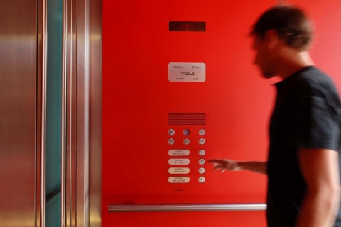 Mann betätigt Knopf eines Schindler-Fahrstuhls. Die Innenseite ist knallrot, sowie die Beschriftung der weißen Knöpfe