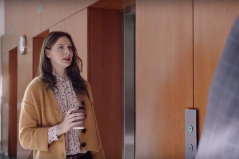 Frau mit Kaffeebecher vor einem Aufzug