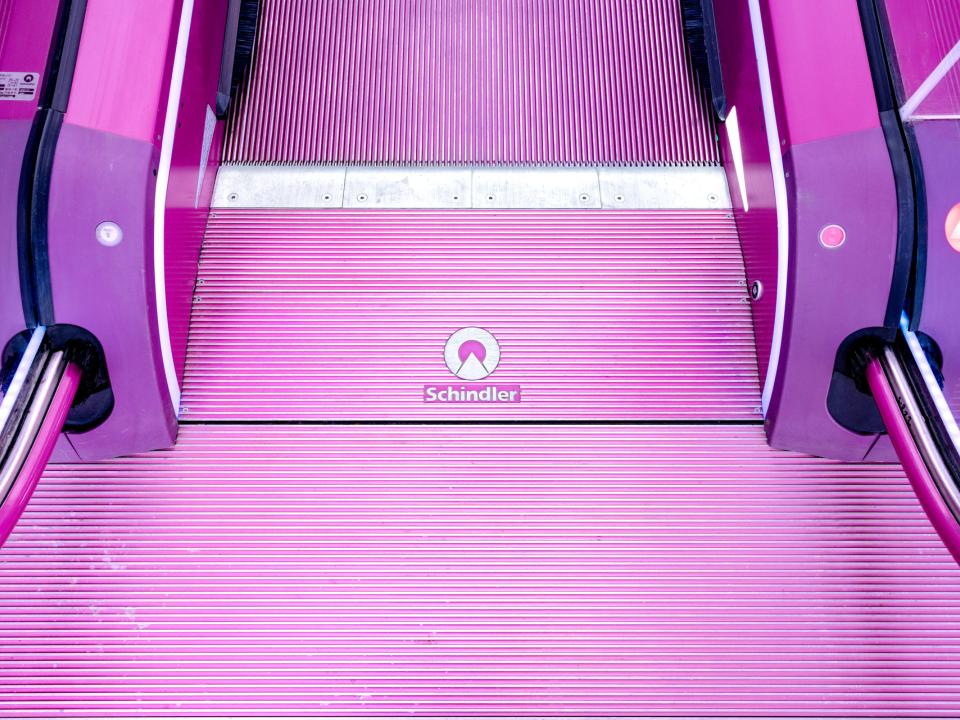 Nahaufnahme eines pinken Schindler-Rolltreppenabsatzes mit strukturierten Stufen.____