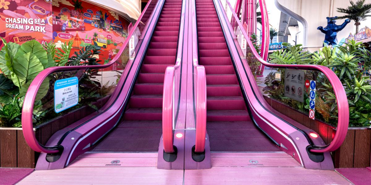 Breite Ansicht einer pinken Rolltreppe in einem Einkaufszentrum mit grünen Pflanzen.